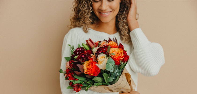A cheerful woman holds a vibrant bouquet of orange and red flowers, radiating joy.