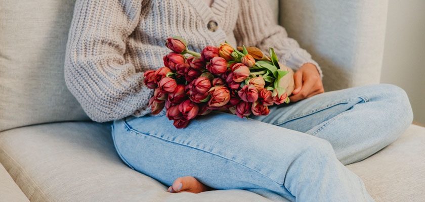 A cozy scene featuring a person in a knitted sweater holding a bouquet of vibrant tulips.