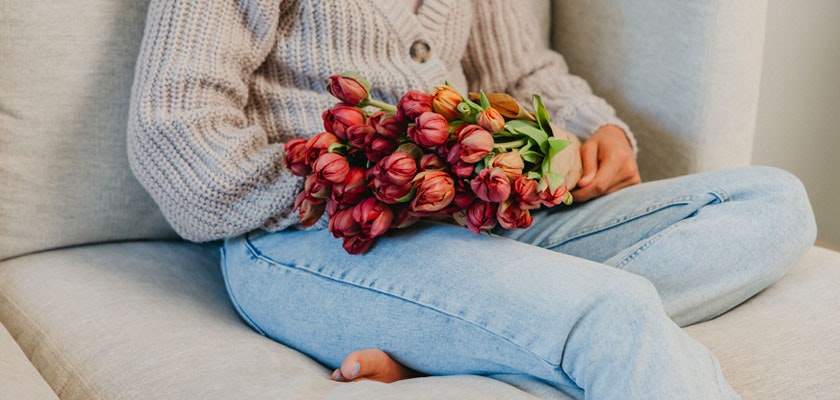 A cozy scene featuring a person in a knitted sweater holding a bouquet of vibrant tulips.