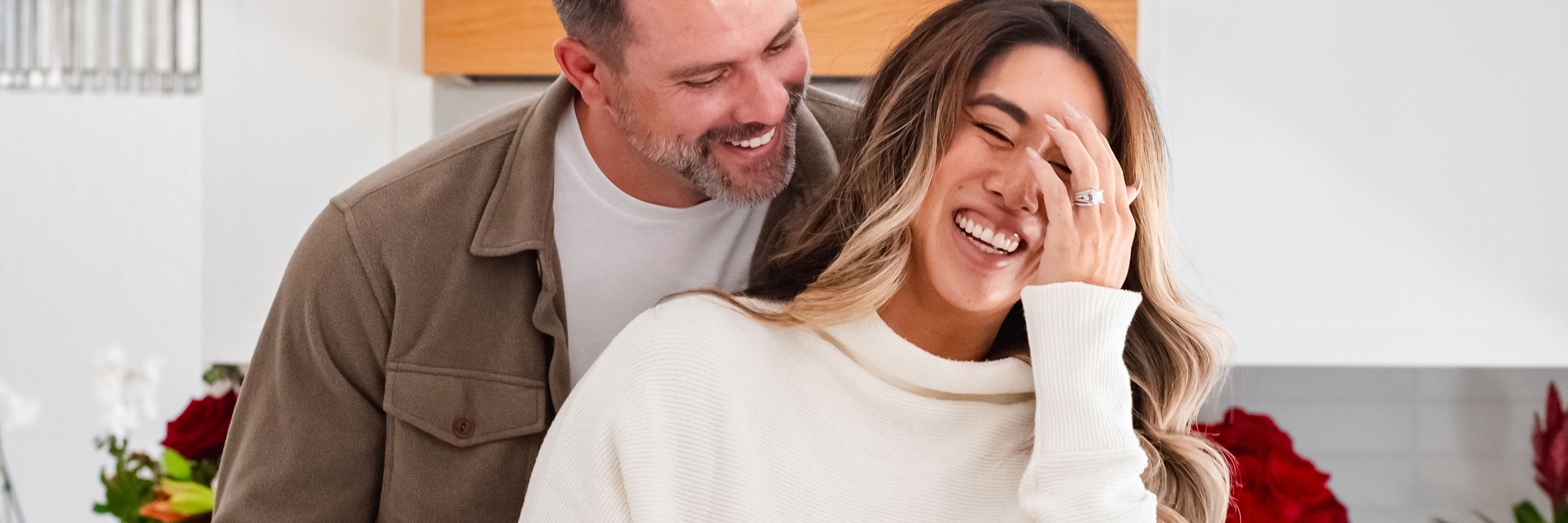 Cheerful couple sharing a joyful moment in a cozy kitchen, surrounded by beautiful roses.