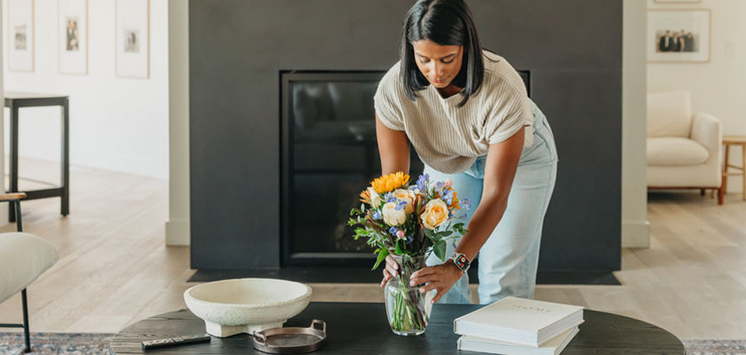 A woman arranging a colorful bouquet of flowers in a glass vase on a stylish coffee table.
