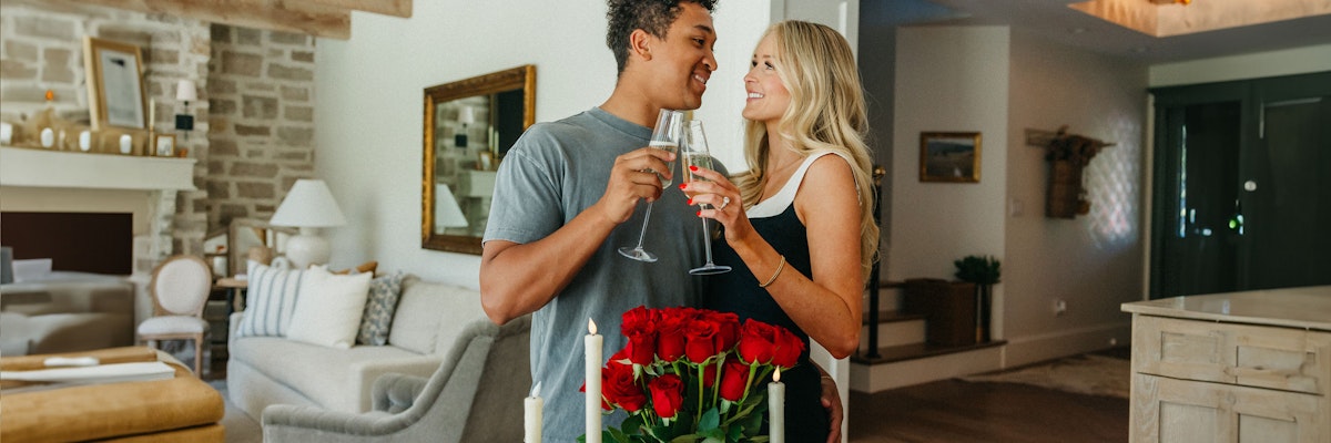 A couple celebrating with champagne and a romantic bouquet of red roses in a cozy home setting.