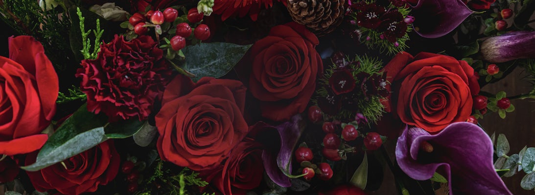 Elegant floral arrangement featuring deep red roses, purple calla lilies, and rich greenery.