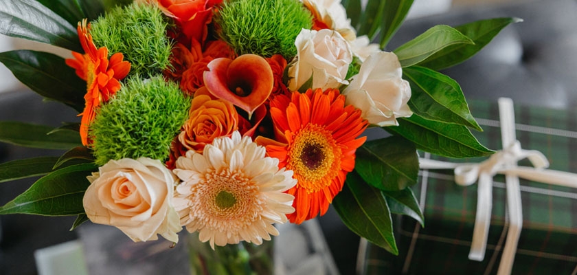 Vibrant floral bouquet featuring orange gerberas, roses, and lush greenery in a stylish arrangement.