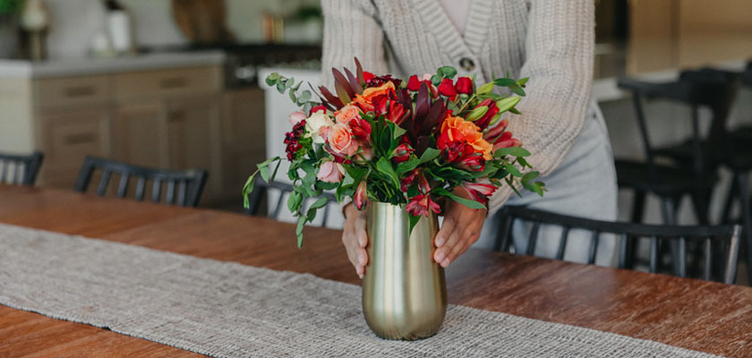Vibrant floral arrangement in a golden vase, set on a rustic dining table.