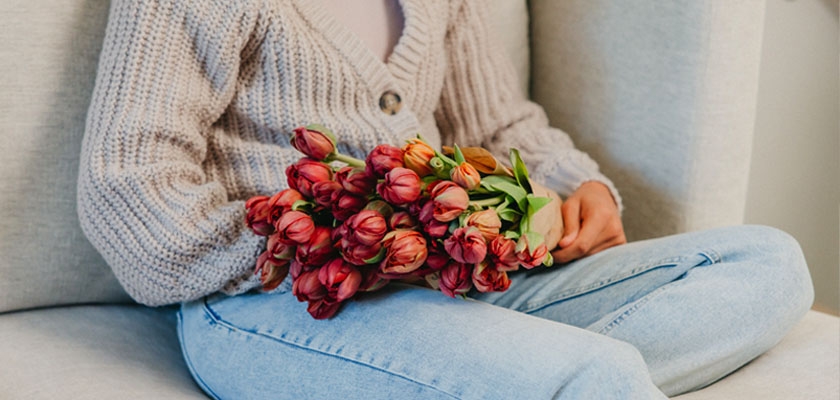 A cozy scene featuring a person holding a bouquet of vibrant red tulips, elegantly styled.
