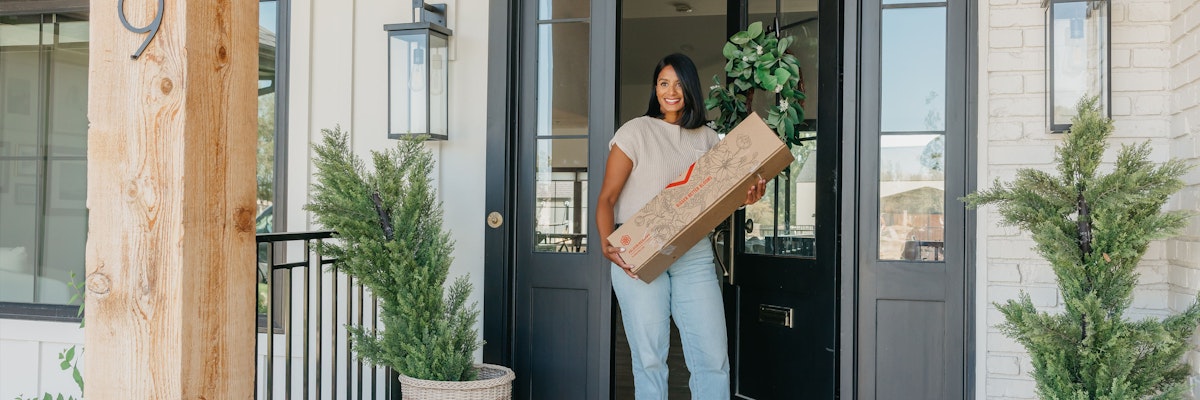 A happy woman receiving a floral delivery at her front door, surrounded by greenery.
