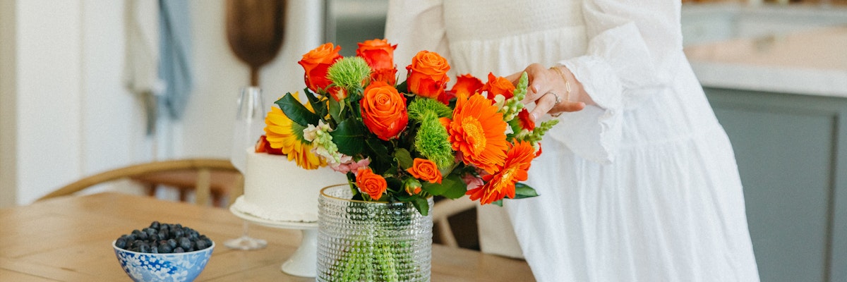 Vibrant floral arrangement featuring orange roses, sunflowers, and green accents in a glass vase.