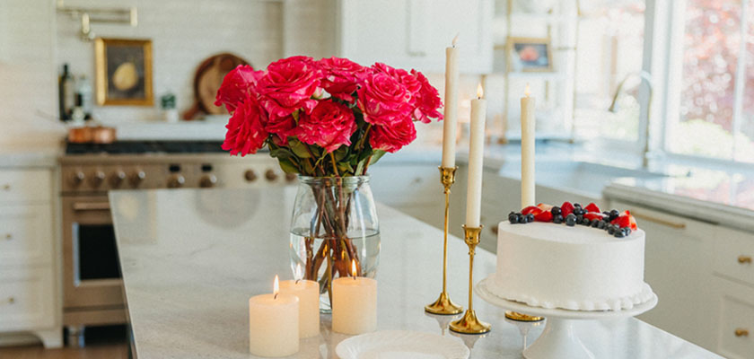 Vibrant pink roses in a vase beside a white cake and candles, enhancing a cheerful kitchen setting.