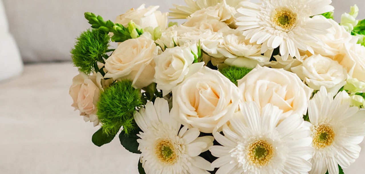 Elegant white flower arrangement featuring roses, gerberas, and vibrant green accents in a stylish bouquet.