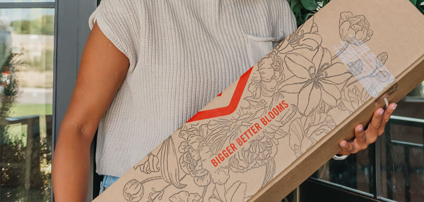 A woman holding a floral delivery box featuring a stylish design, ready to brighten her day.