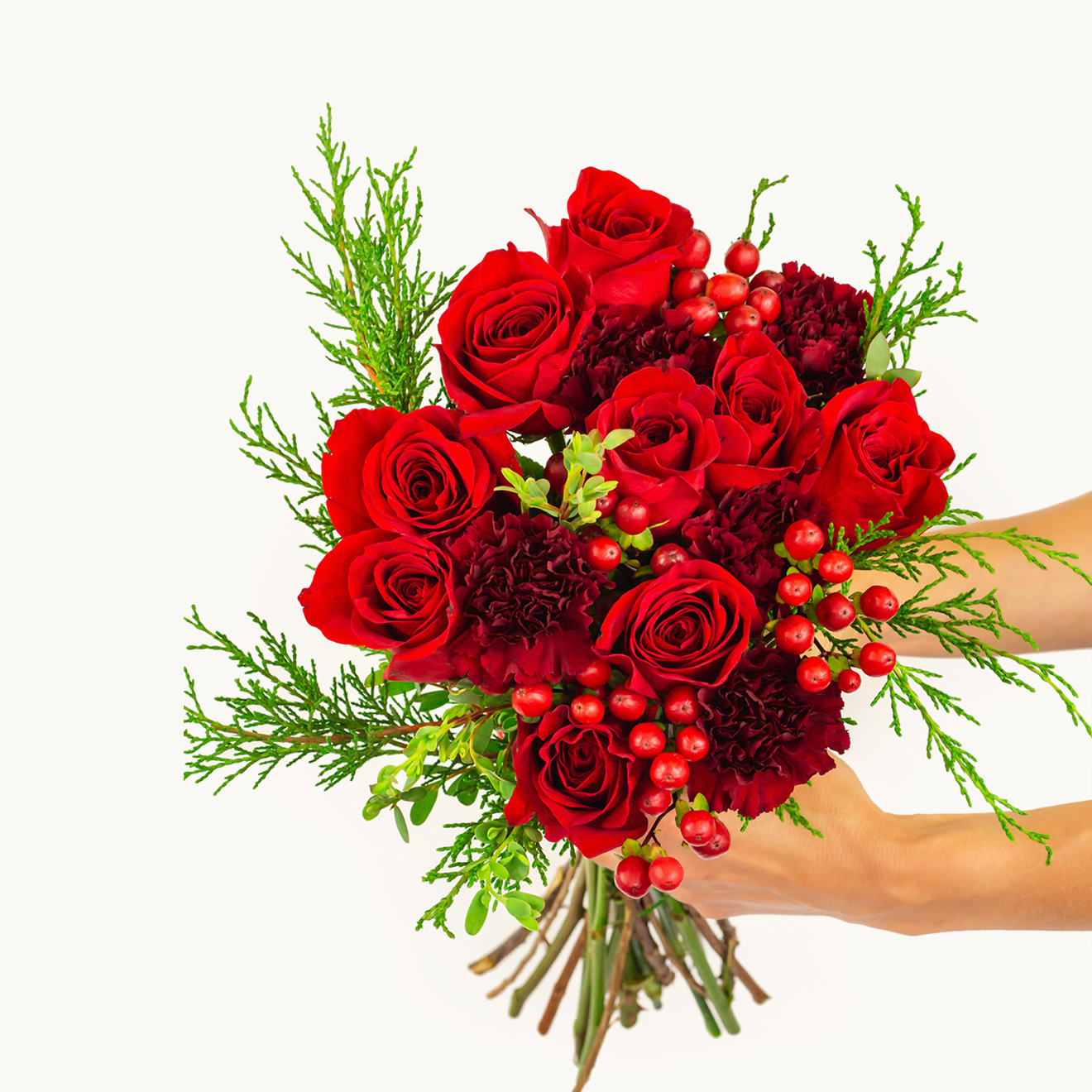 Handcrafted bouquet featuring vibrant red roses, festive greenery, and seasonal berries.