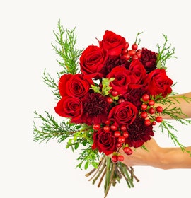 Handcrafted bouquet featuring vibrant red roses, festive greenery, and seasonal berries.