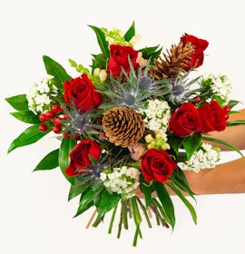 Vibrant bouquet featuring red roses, greenery, and pinecones, perfect for festive occasions.