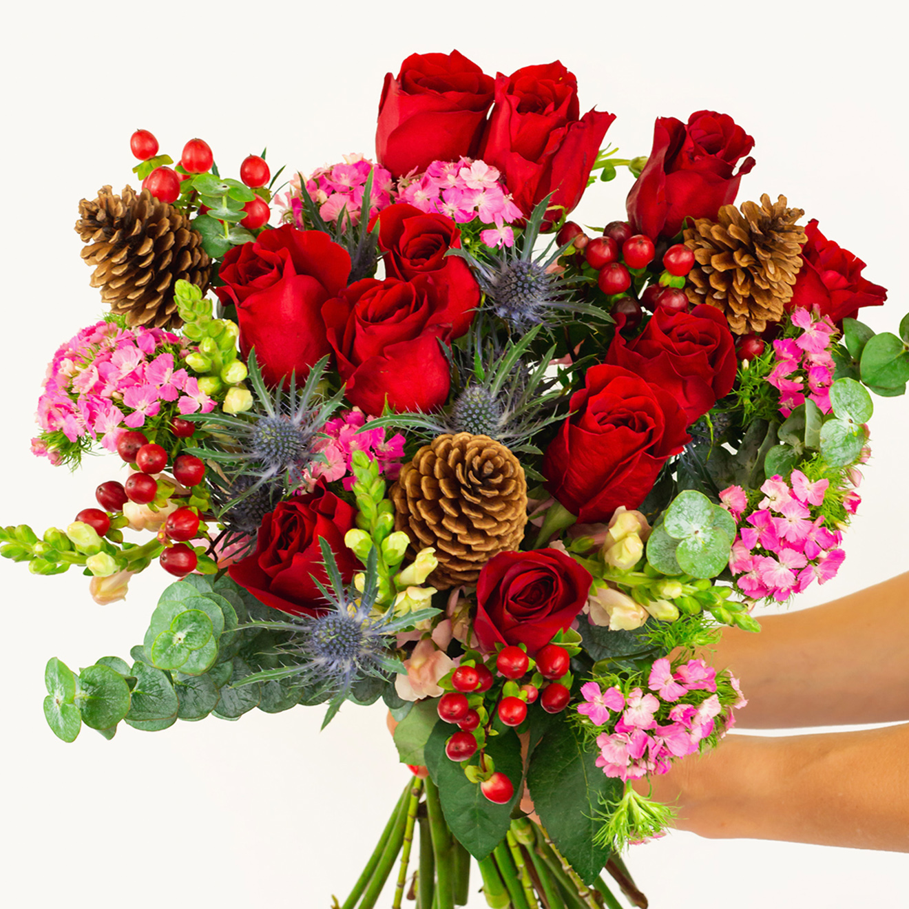 Vibrant bouquet featuring red roses, pink blooms, and natural accents like pinecones.