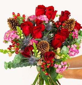 Vibrant bouquet featuring red roses, pink blooms, and natural accents like pinecones.