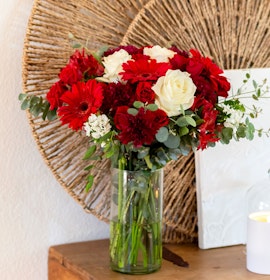 Vibrant floral arrangement featuring red gerbera daisies and white roses in a clear vase.