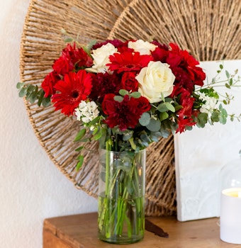 Vibrant floral arrangement featuring red gerbera daisies and white roses in a clear vase.