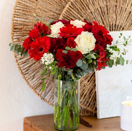 Vibrant floral arrangement featuring red gerbera daisies and white roses in a clear vase.