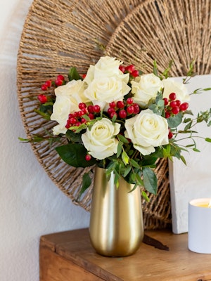 Elegant white roses with red berries arranged in a stylish gold vase, perfect for home décor.