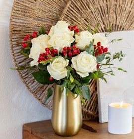 Elegant white roses with red berries arranged in a stylish gold vase, perfect for home décor.