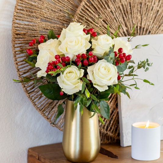 Elegant white roses with red berries arranged in a stylish gold vase, perfect for home décor.