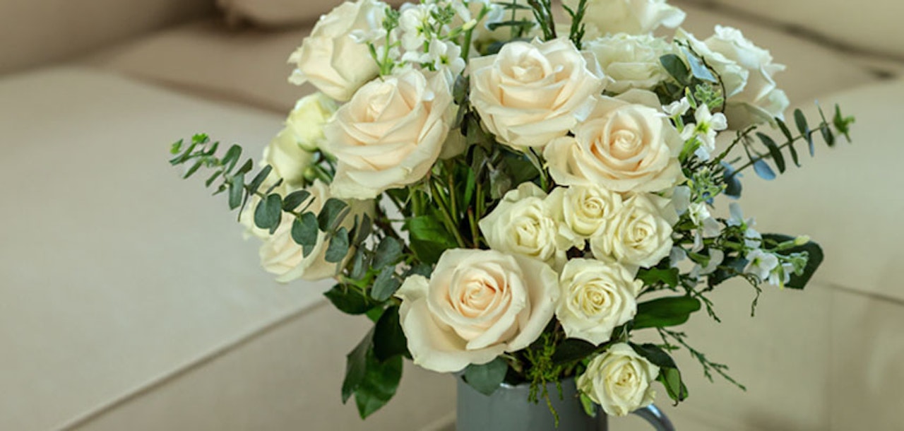 Elegant bouquet of cream roses and white blooms, styled in a rustic vase for a chic decor.