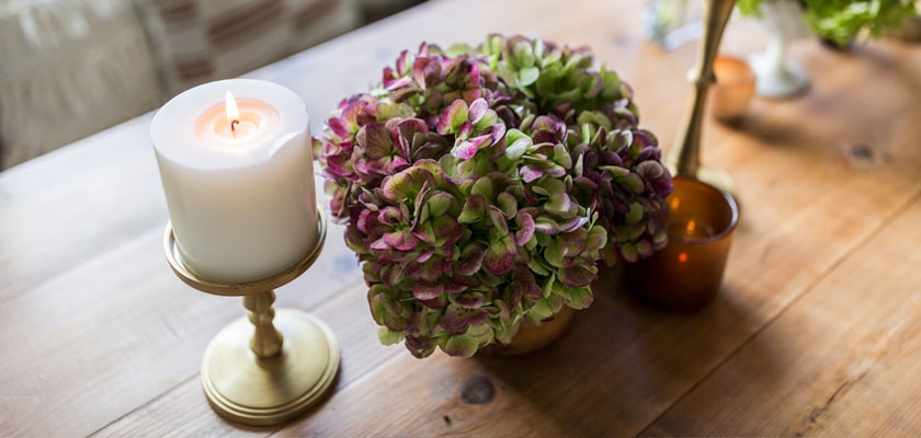 A lush arrangement of green and purple hydrangeas beside a softly glowing candle.