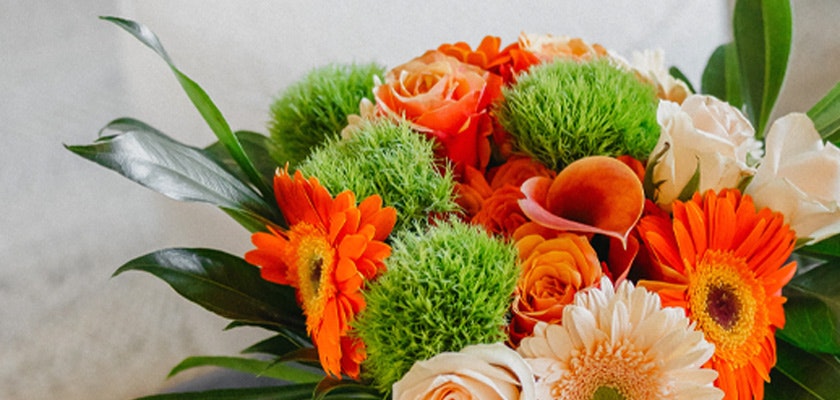 Vibrant floral arrangement featuring orange roses, green blooms, and cheerful gerbera daisies.