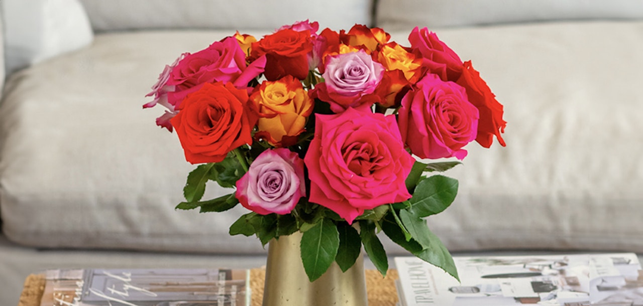 Vibrant rose bouquet featuring shades of red, pink, and orange in a stylish vase.