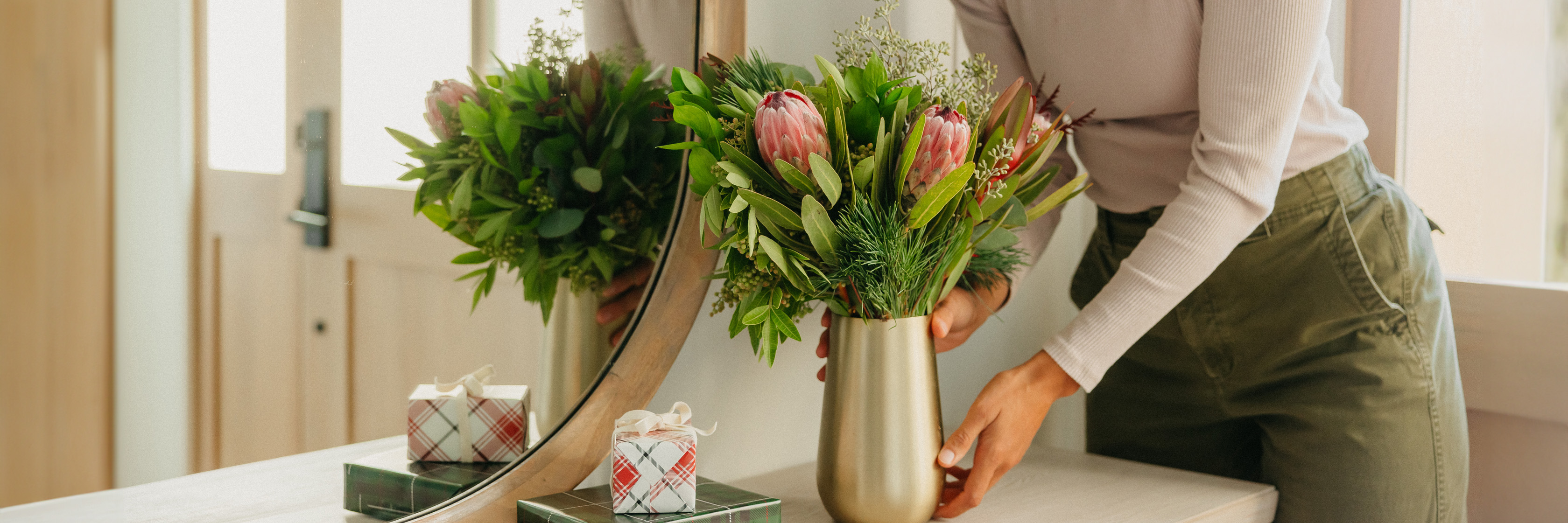 A stylish woman arranges a chic floral centerpiece next to decorative gifts on a modern table.