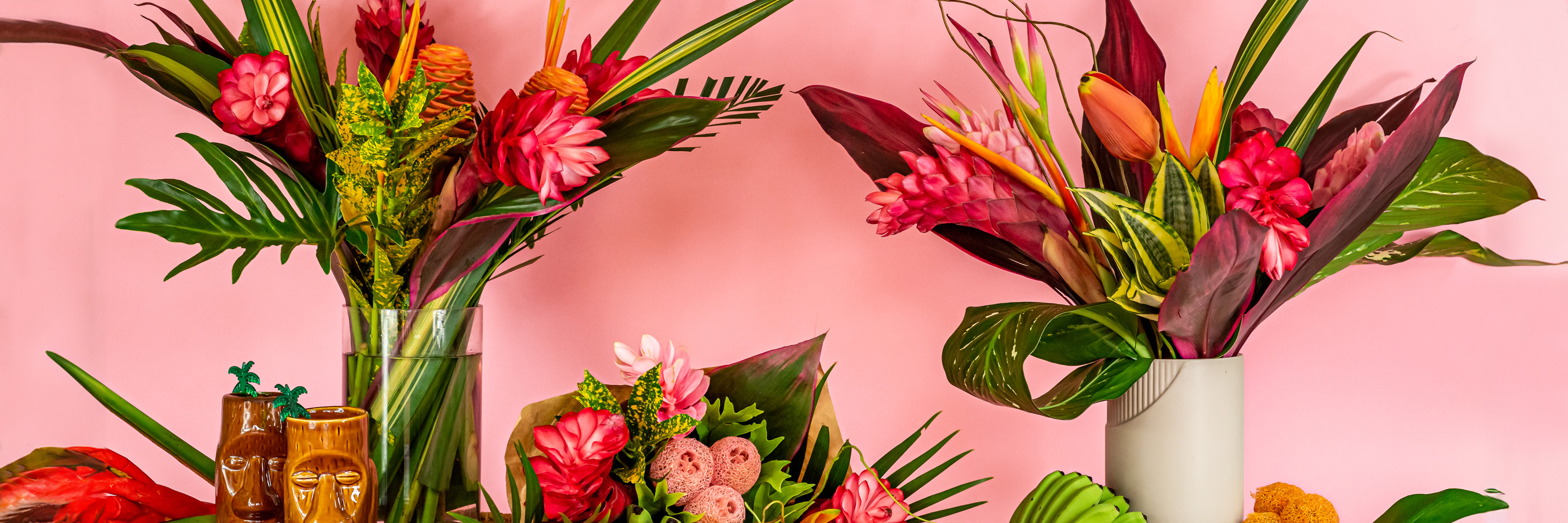 Vibrant floral arrangement featuring tropical flowers in stylish vases against a pink backdrop.