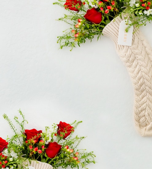 Charming holiday floral arrangement with red roses and greenery in a cozy knitted stocking.