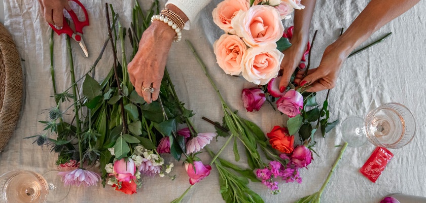 An overhead view of hands arranging colorful flowers on a linen table, showcasing creativity.