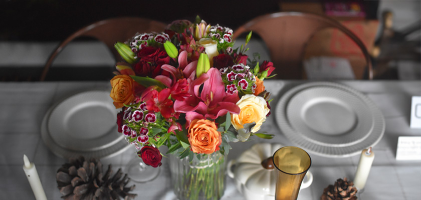 Vibrant floral centerpiece featuring roses, lilies, and mixed blooms on a dining table setting.