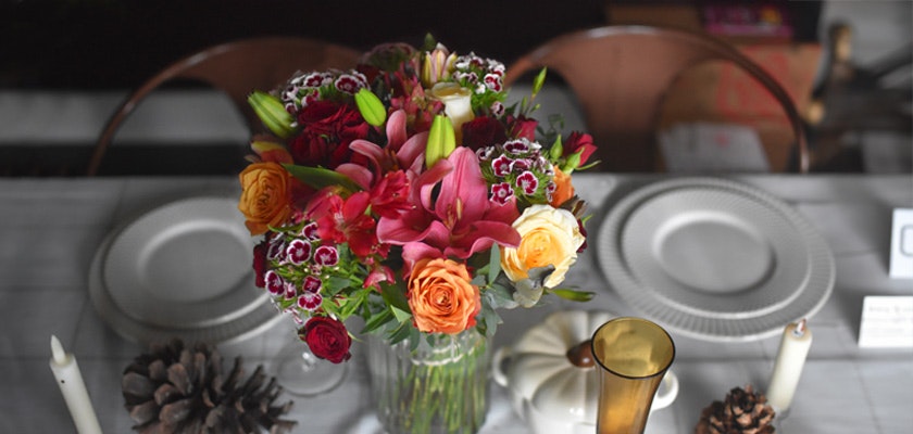 Vibrant floral centerpiece featuring roses, lilies, and mixed blooms on a dining table setting.