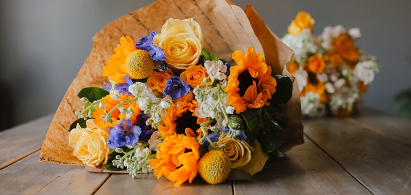 Vibrant bouquet featuring sunflowers, yellow roses, and blue blooms, wrapped elegantly.