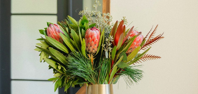 Vibrant bouquet featuring proteas, greenery, and elegant foliage in a stylish vase.