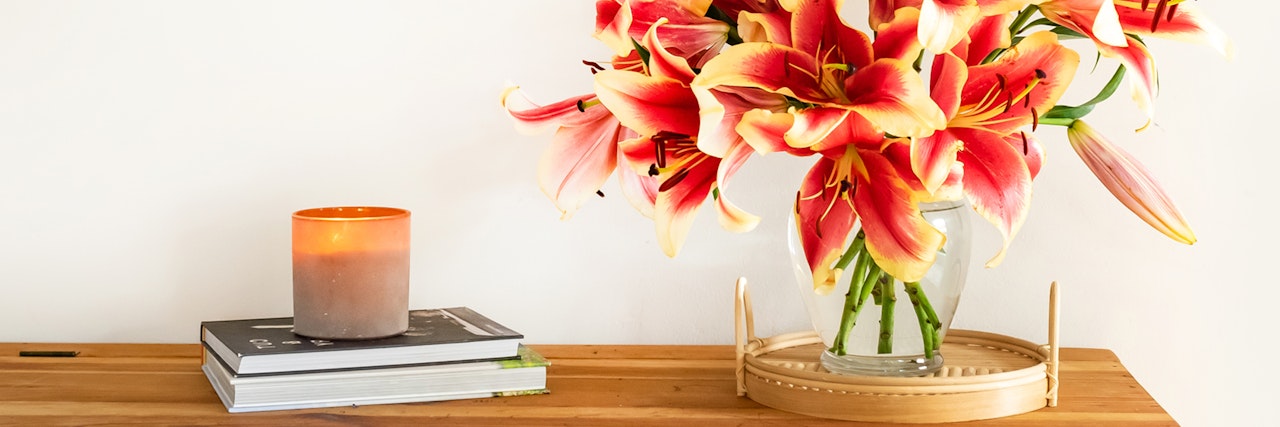 Vibrant bouquet of red and yellow lilies in a glass vase on a wooden table.