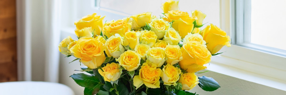 Bright bouquet of yellow roses in varying shades, elegantly displayed by a sunny window.
