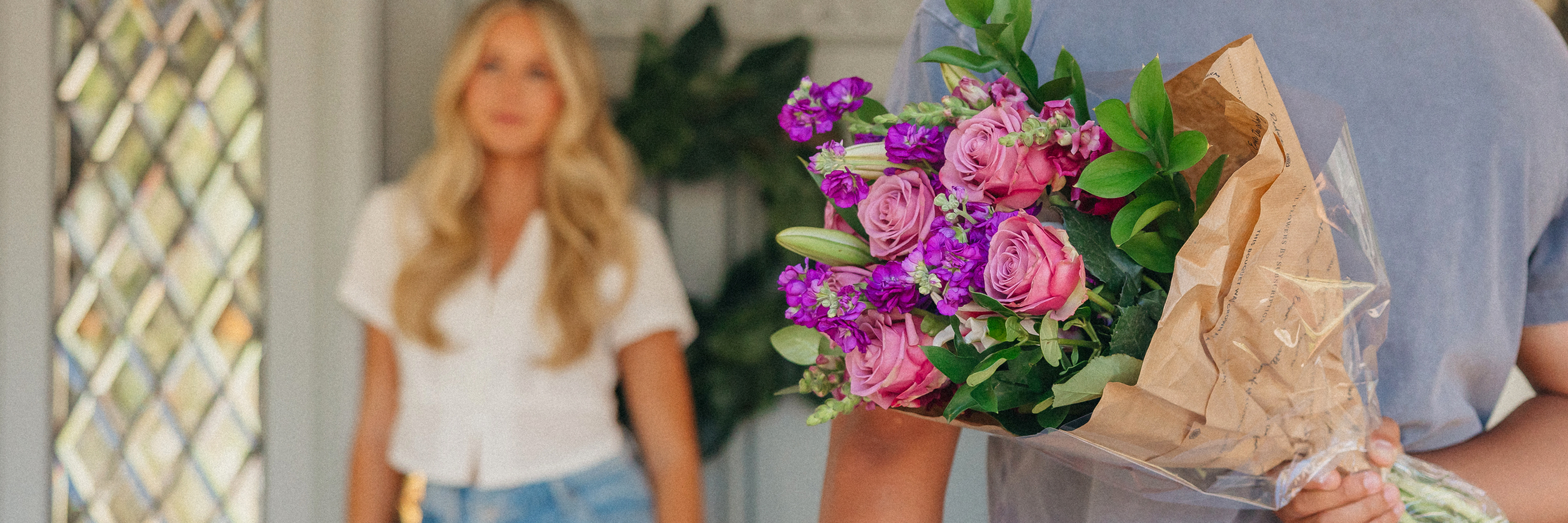 A vibrant bouquet of pink roses and purple flowers held by a person, with a blurred background.