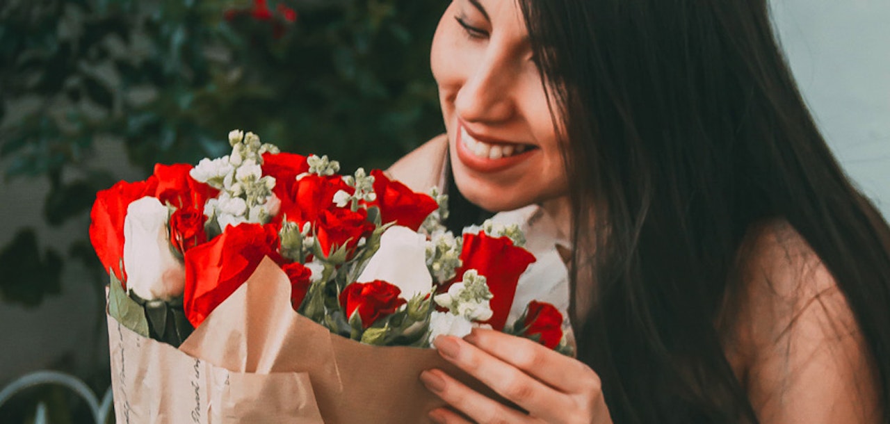A smiling woman joyfully holds a vibrant bouquet of red and white roses, accents of greenery included.