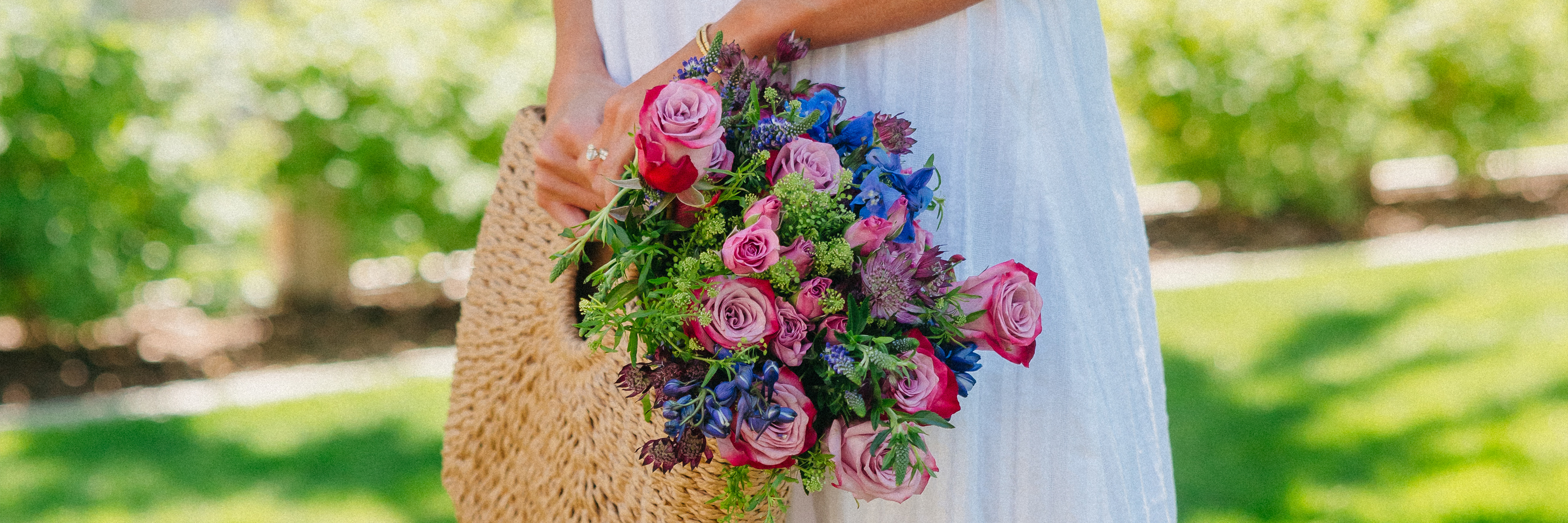 A vibrant bouquet of pink roses and blue blooms held by a woman outdoors, perfect for celebrations.