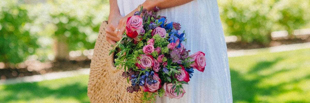 A vibrant bouquet of pink roses and blue blooms held by a woman outdoors, perfect for celebrations.