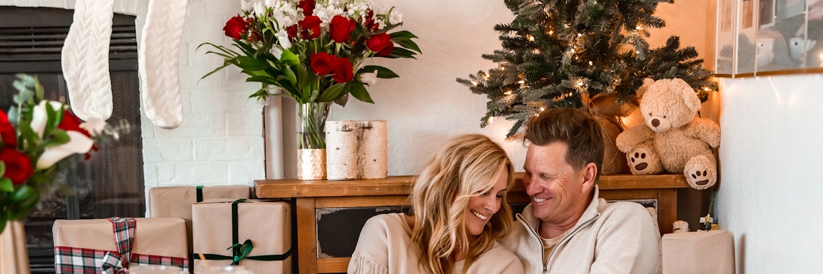 Cozy holiday scene with a couple by a fireplace, surrounded by gifts and festive decor.