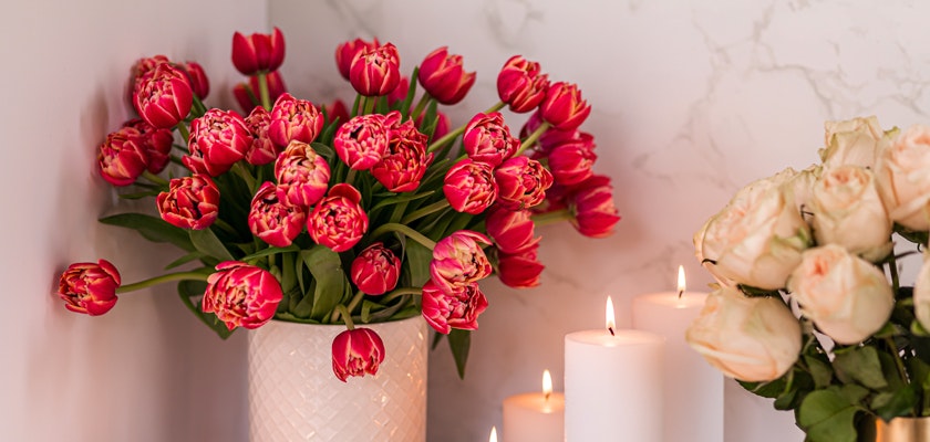Vibrant bouquet of red tulips in a decorative vase, accented by soft candles and pale roses.
