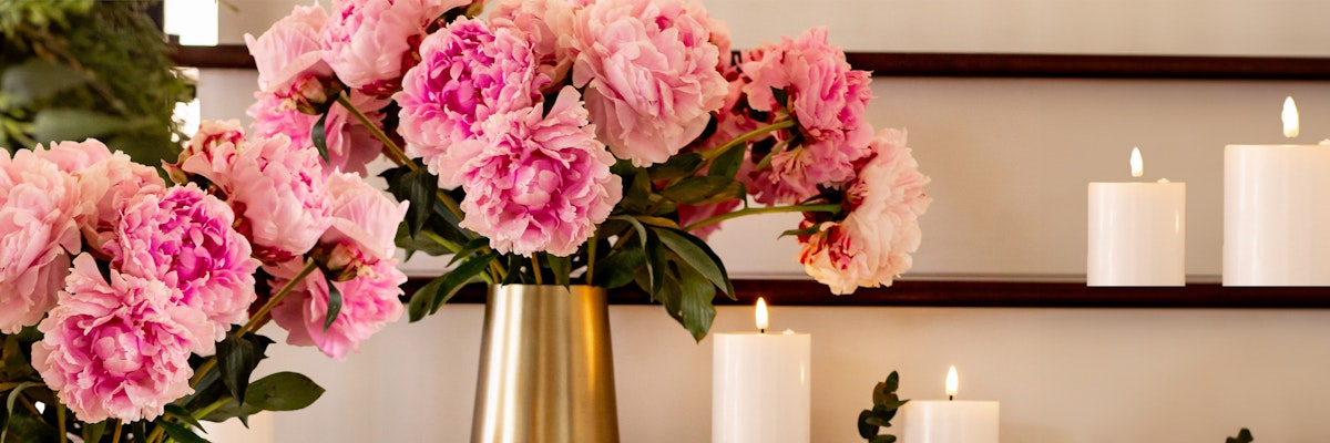 Elegant pink peonies in a gold vase complemented by flickering white candles for a serene setting.