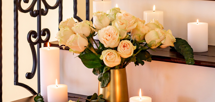 Elegant white roses in a golden vase, surrounded by glowing candles, creating a serene atmosphere.
