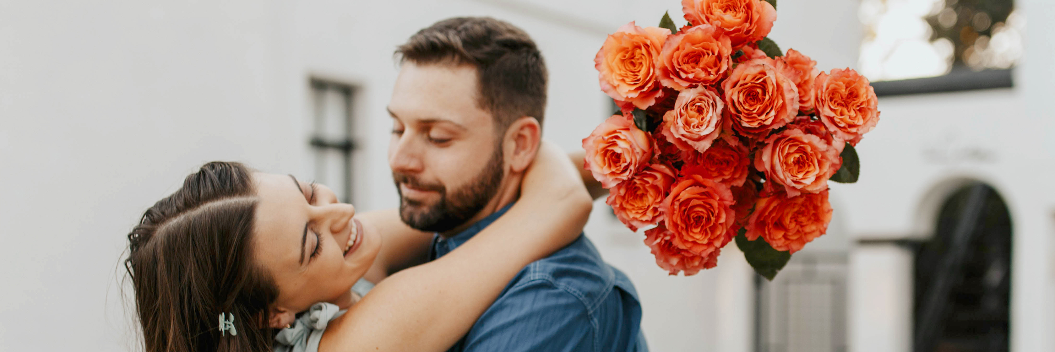 A romantic couple embracing, with a vibrant bouquet of orange roses adding a loving touch.