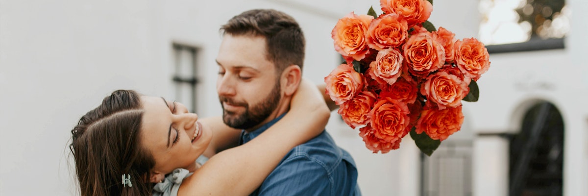 A romantic couple embracing, with a vibrant bouquet of orange roses adding a loving touch.
